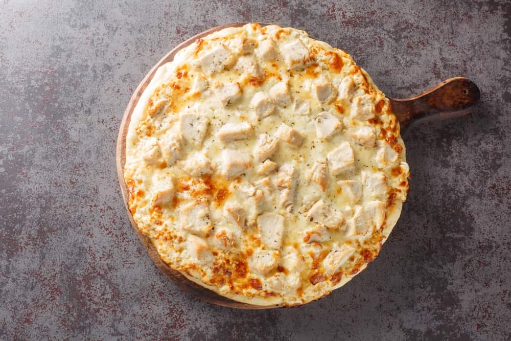 Parmesan Crusted Chicken Alfredo Pizza closeup on the wooden board on the table. Horizontal top view from above