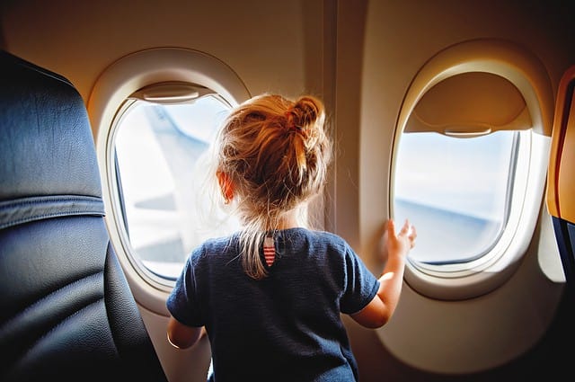 Adorable little girl traveling by an airplane. Child sitting by aircraft window and looking outside. Traveling with kids abroad. Family on summer vacations.