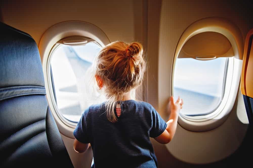 Adorable little girl traveling by an airplane. Child sitting by aircraft window and looking outside. Traveling with kids abroad. Family on summer vacations.