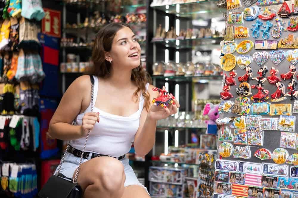 Woman peruses selection of of memorable gifts at shop in popular tourist destination. She carefully examines various items, picking up souvenir magnet