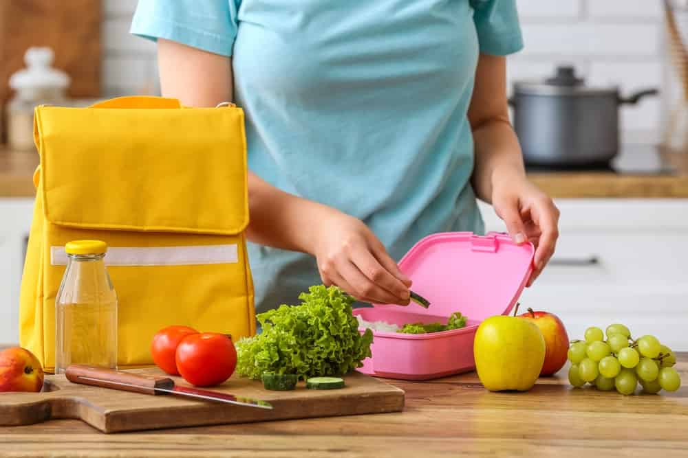 Woman packing fresh meal into lunch box in kitchen