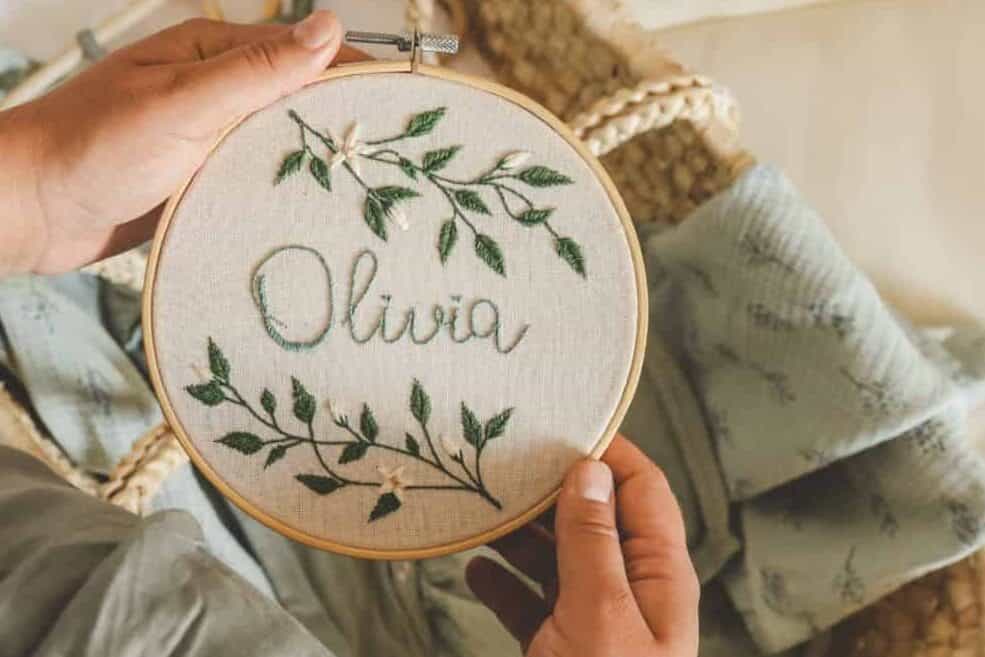 Pregnant woman holding a handmade embroidery with the name Olivia in her hands, concept in anticipation.