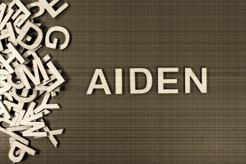 Popular and modern baby boy fashion name AIDEN in wooden English language capital letters spilling from a pile of letters on a green background in sepia