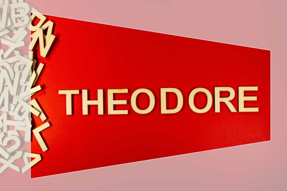 Popular and modern baby boy fashion name THEODORE in wooden English language capital letters spilling from a pile of letters on a red background framed