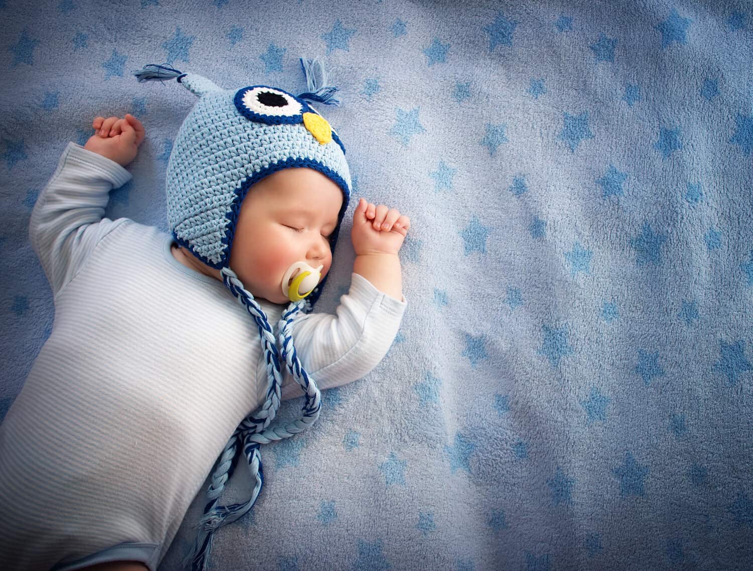 4 month old baby in owl hat sleeping on blue blanket