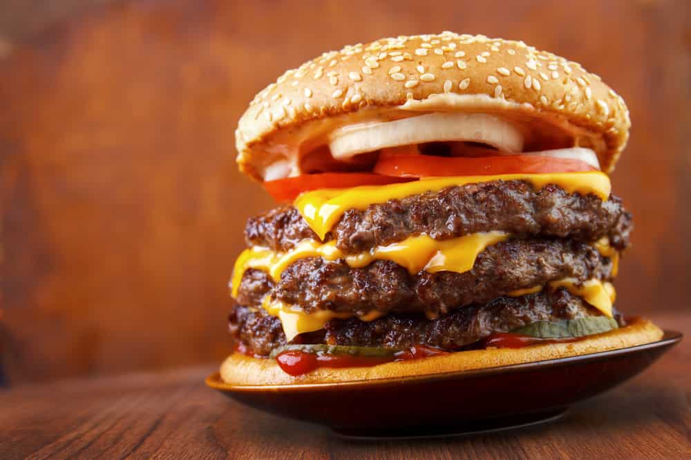 Big beef burger with three patties and cheese on plate , wood background