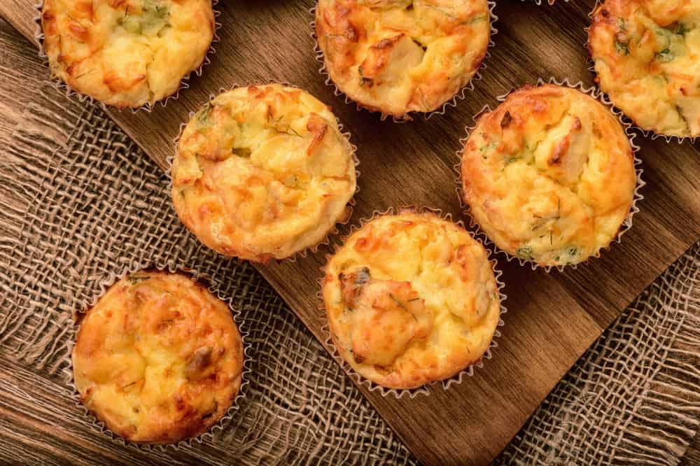 Homemade muffins with chicken and cheese on brown wooden board.