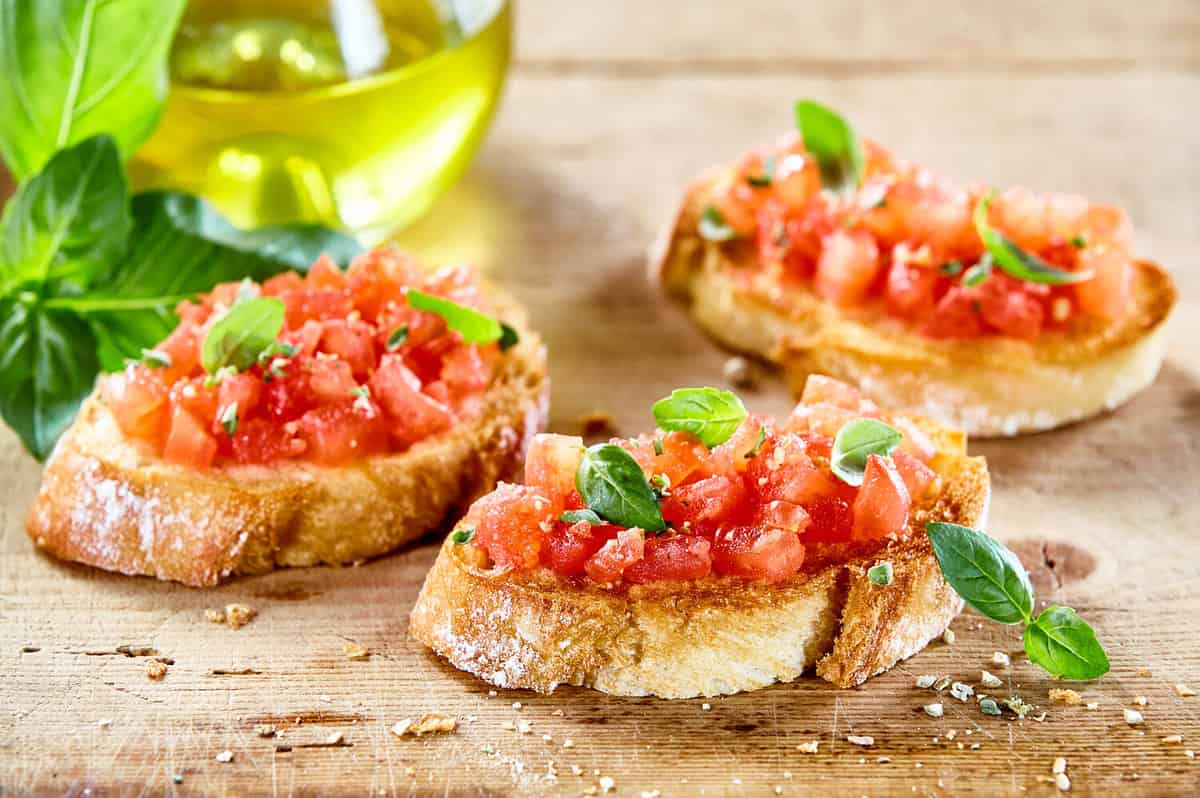 Tasty savory tomato Italian appetizers, or bruschetta, on slices of toasted baguette garnished with basil, close up on a wooden board
