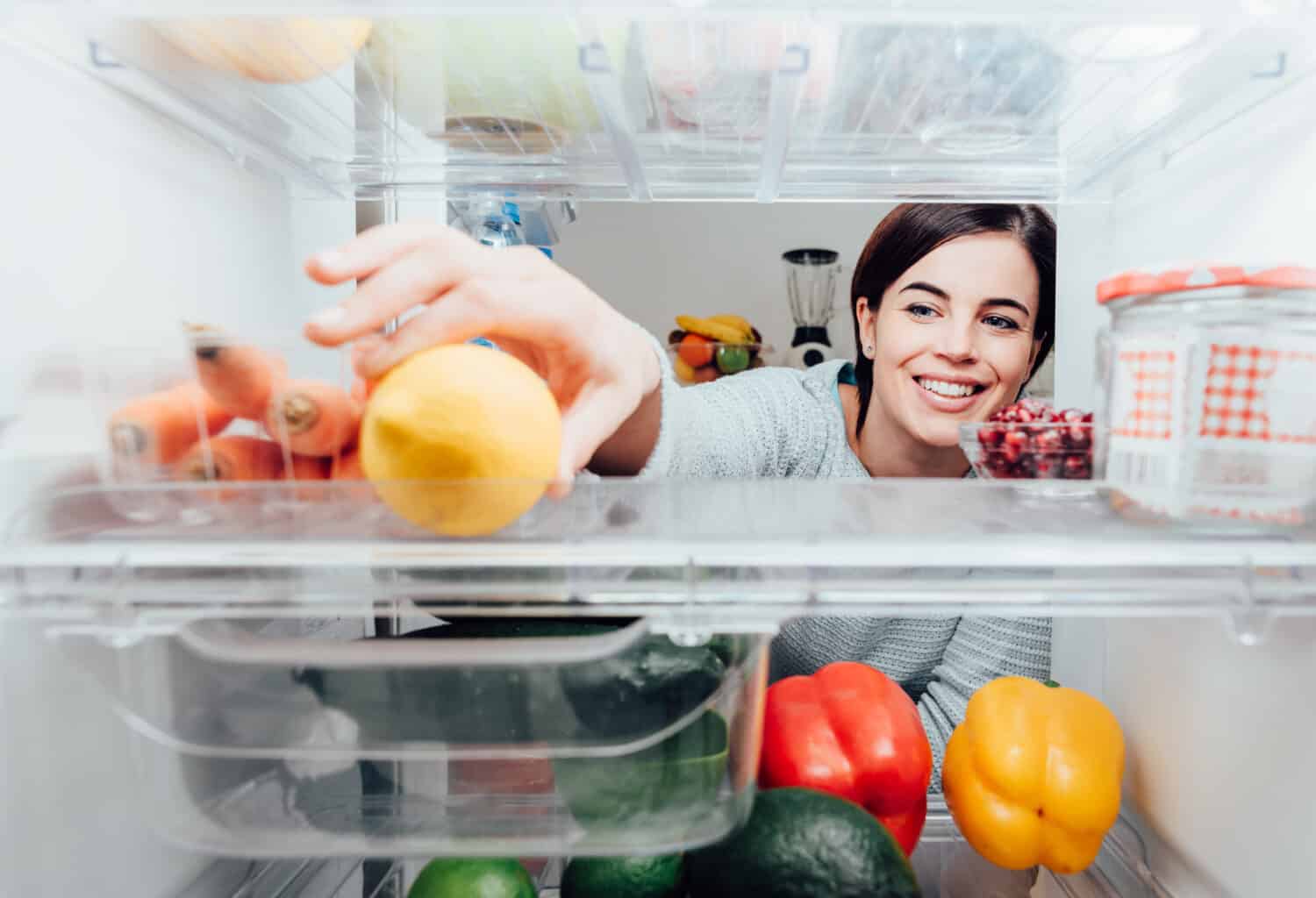 Smiling woman taking a fresh lemon out of the fridge, healthy food concept