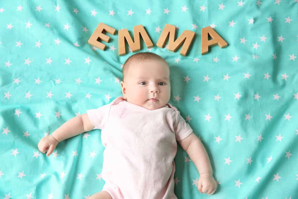 Cute baby with word EMMA lying on bed. Choosing name concept