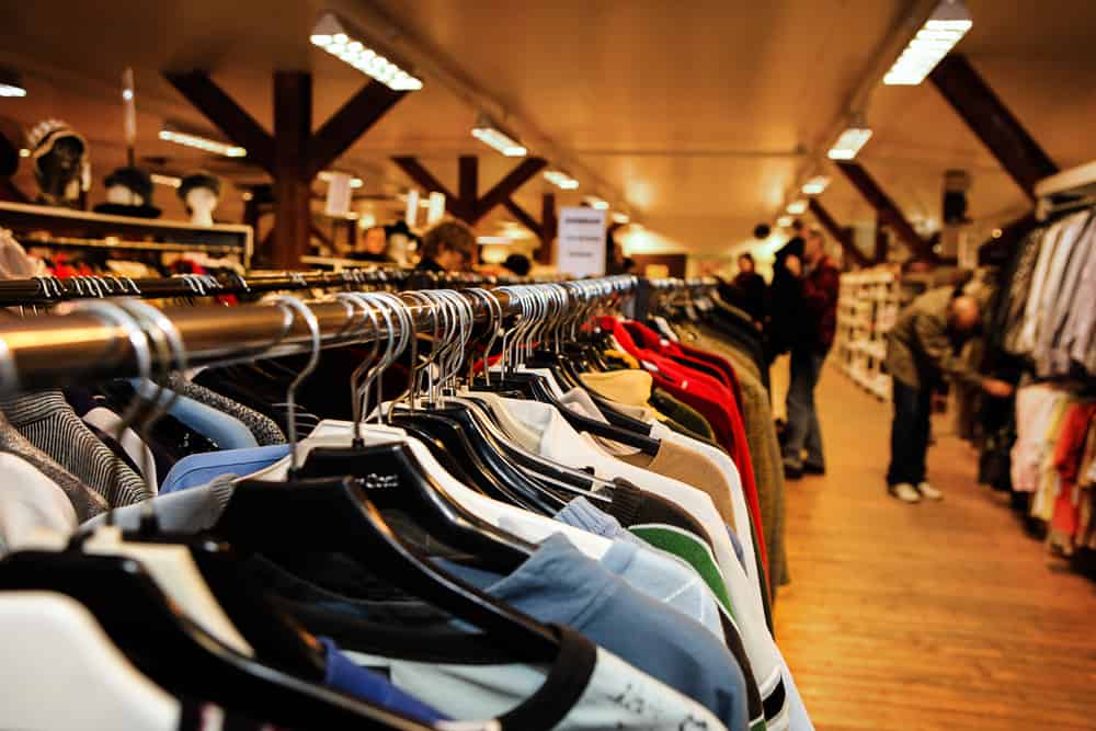 Used clothes on hangers in a thrift store. Out off focus, anonymous customers are seen in the background.