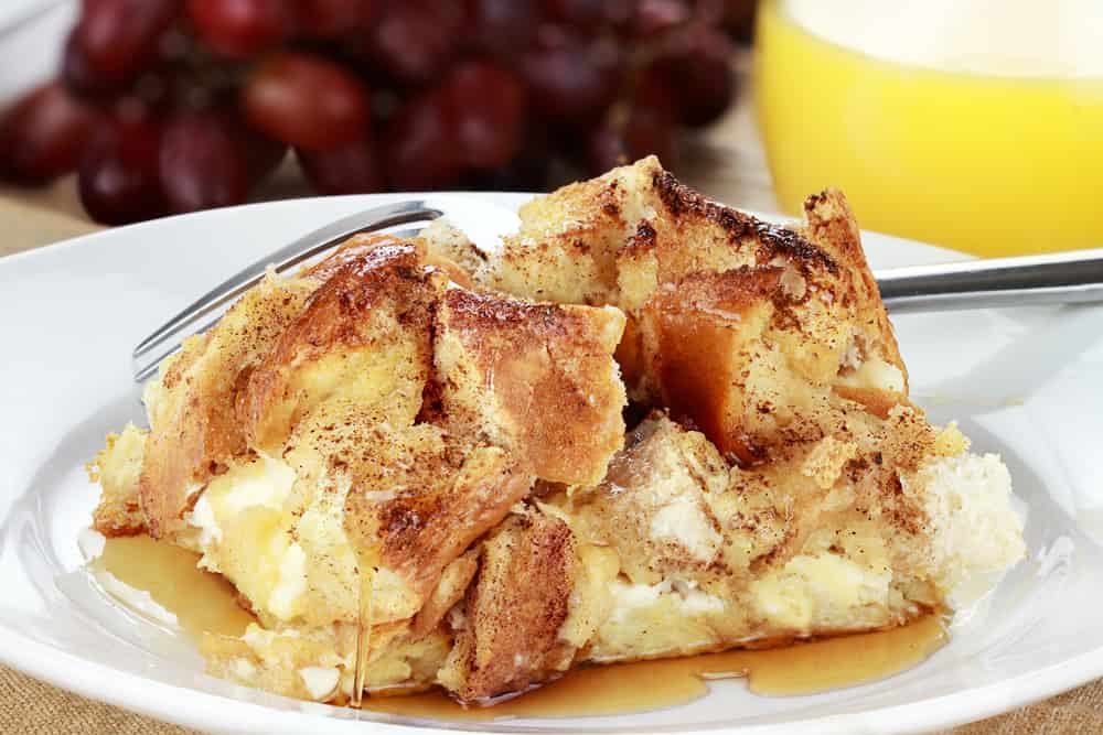 French toast casserole with maple syrup. Made with cream cheese cheese in the center. Fresh grapes and orange juice in background. Extreme shallow depth of field with selective focus on French toast.