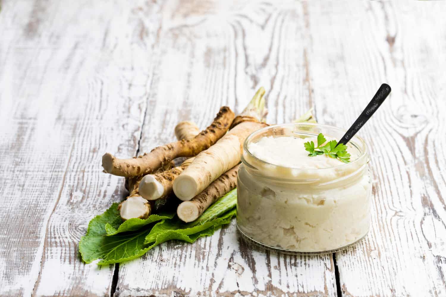 Spicy  horseradish sauce in small glass jar on wooden table 