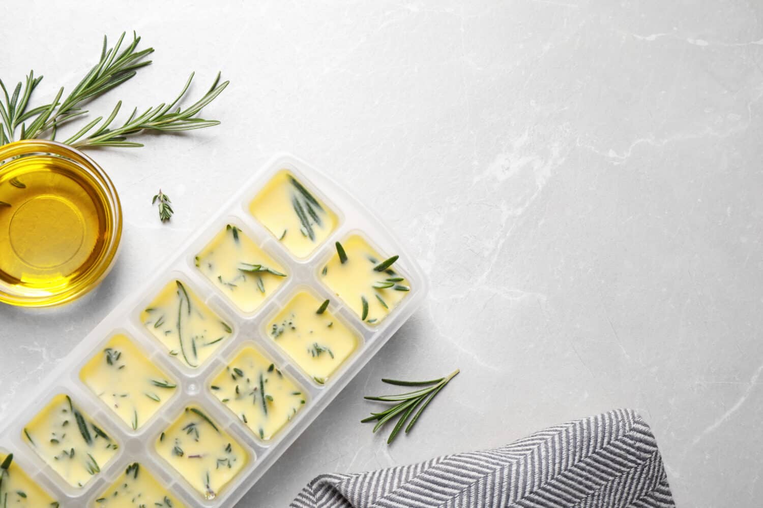 Ice cube tray with herbs frozen in oil and fresh rosemary on grey table, flat lay. Space for text