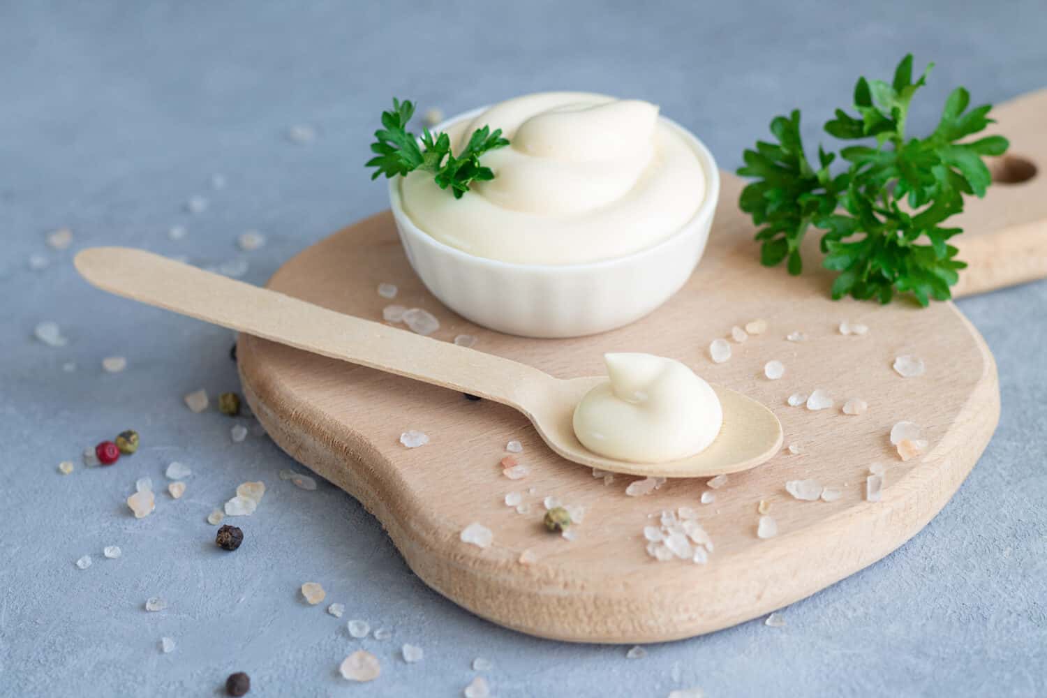 Bowl of fresh organic homemade mayonnaise next to wooden spoon with mayo on wood board