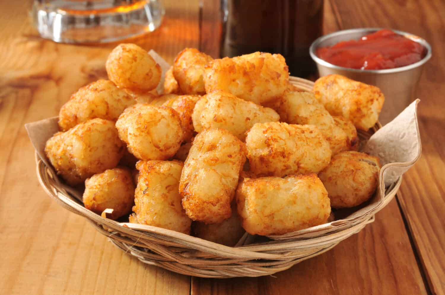 A basket of golden tater tots with beer in the background