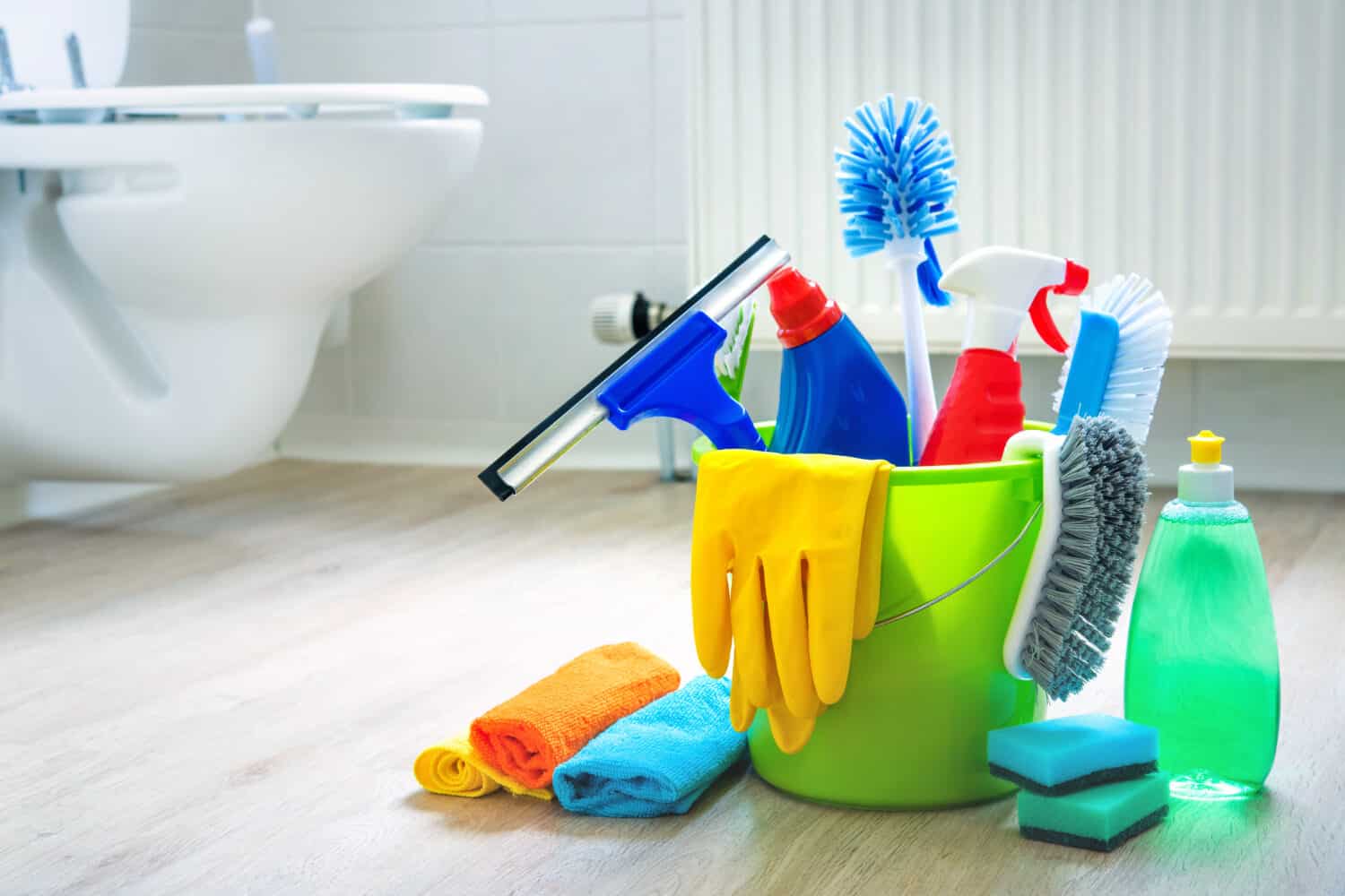 Various cleaning items and supplies in a bucket on the bathroom floor