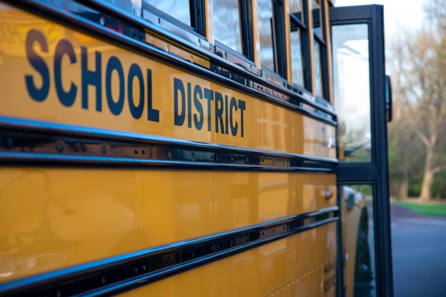 School District written on the side of a school bus. Door is open. No people, nature background.