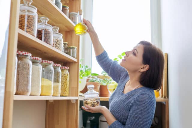 Organization of pantry, woman in kitchen near wooden rack with cans and containers of food