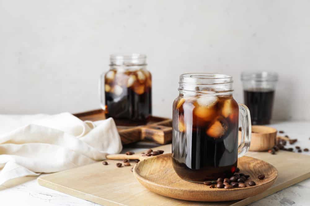 Mason jars of tasty cold brew and coffee beans on white background