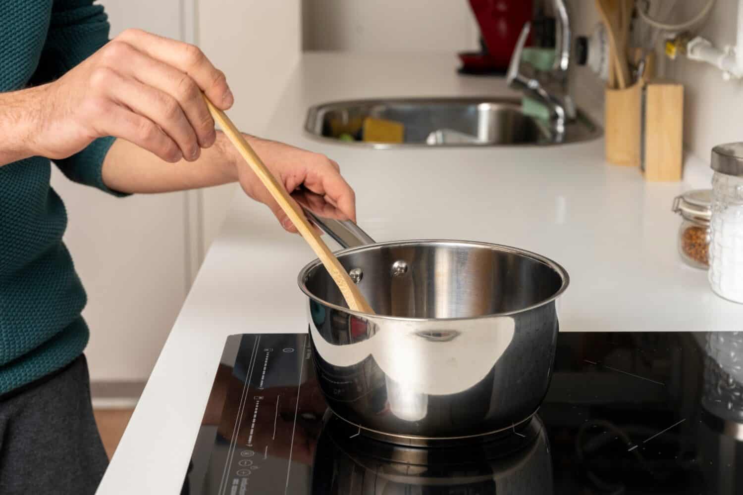 Young man's hands stirring sauce for spaghetti on ceramic hob