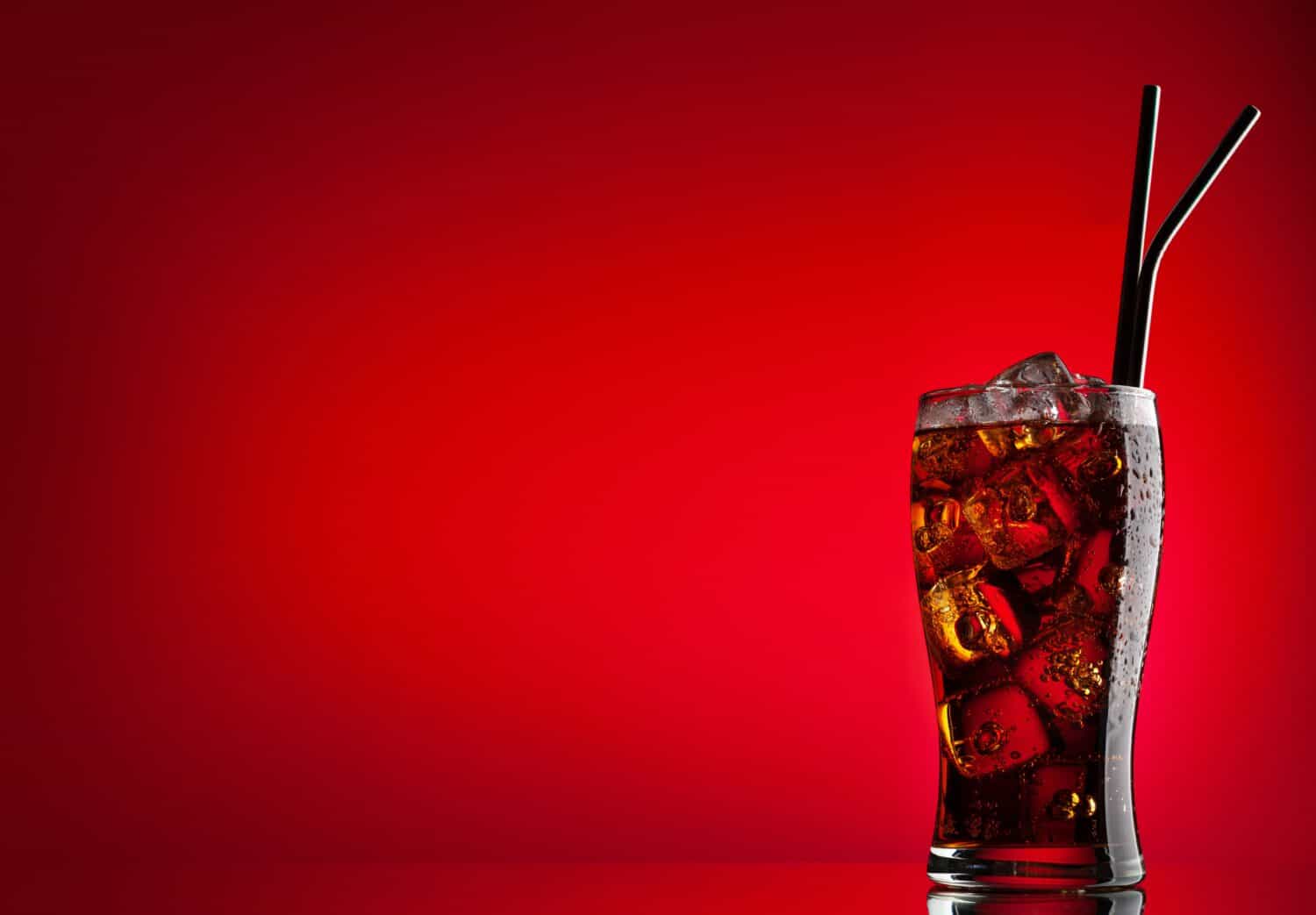 A brown carbonated drink. Fresh cold sweet cola beverage with ice cubes. Over red background with copy space
