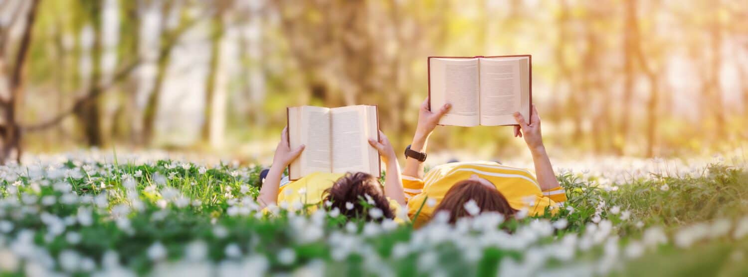 Mother and her son lying down on the beautiful spring field in the sunny park. Concept of the interesting of literature and family leisure.