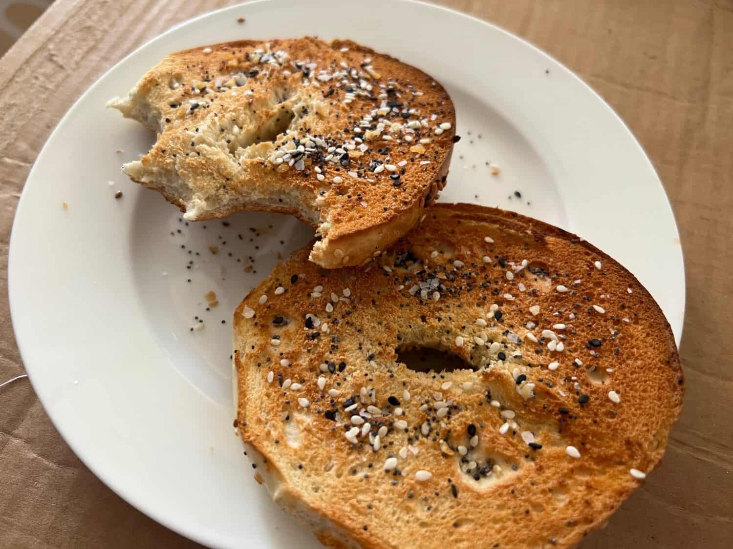 Closeup of plain brown toasted bagel with everything but the bagel seasoning topping, including sesame seeds, poppy seeds, garlic, sea salt.
