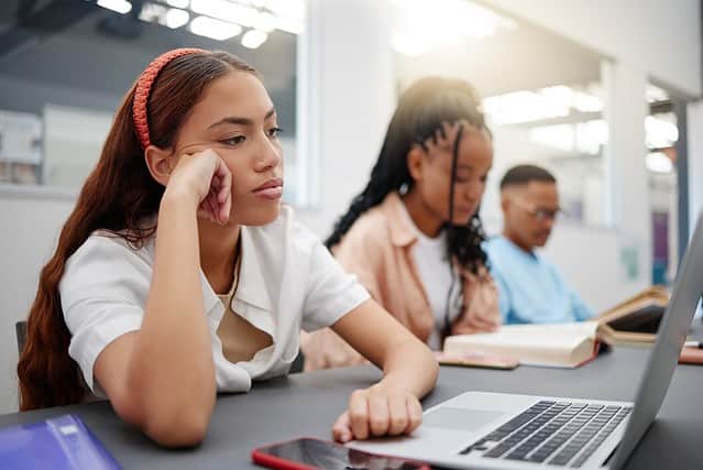 Mental health, studying and student with depression reading course information on laptop in library or university classroom. Sad, depressed and burnout college woman with exam problem or fail results