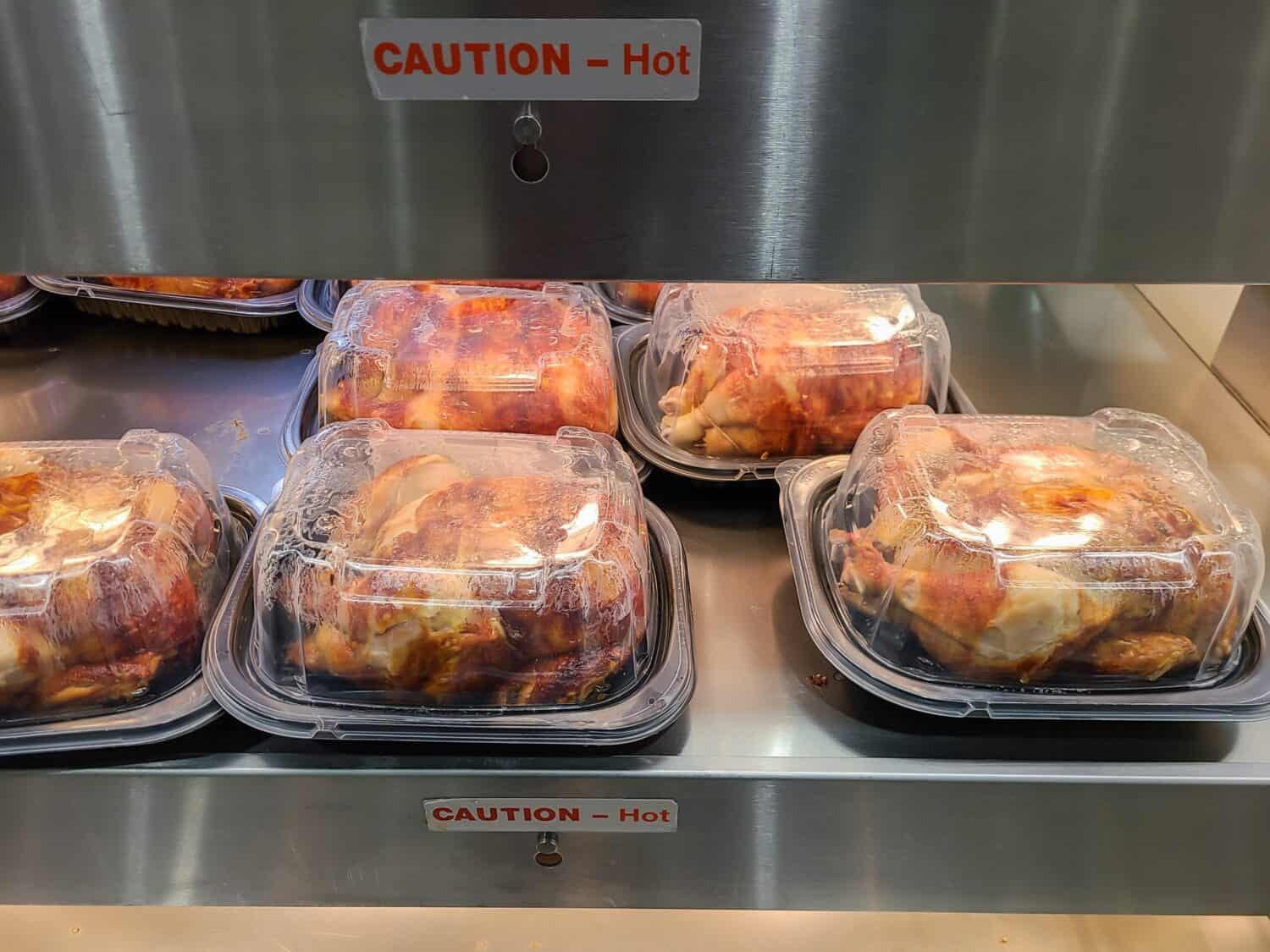 Rotisserie chickens for sale at a Costco store. A sign is visible on the chickens to inform customers that they are hot.