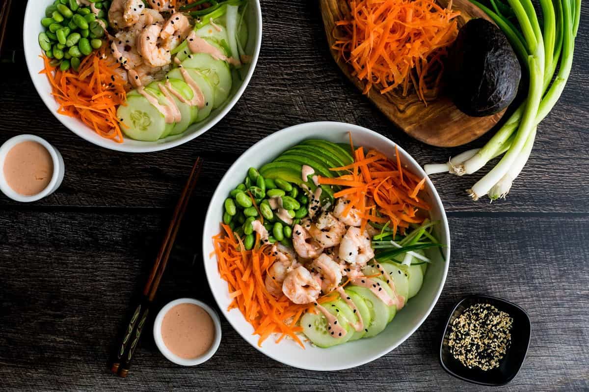 Shrimp Sushi Bowls with Cauliflower Rice and Spicy Mayo: Bowls of shrimp, avocado, carrot, and served as Japanese-style sushi bowls