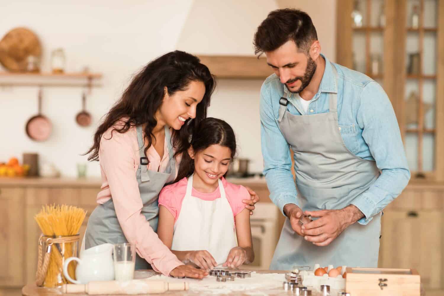 Warm family kitchen scene with mother, father and daughter using cookie cutters on dough, creating nurturing and educational baking experience