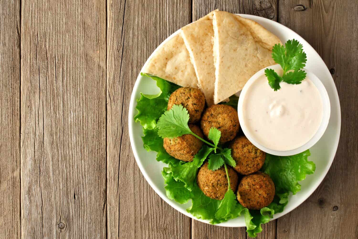 Plate of falafel with pita bread and tzatziki sauce on wooden table. View from above