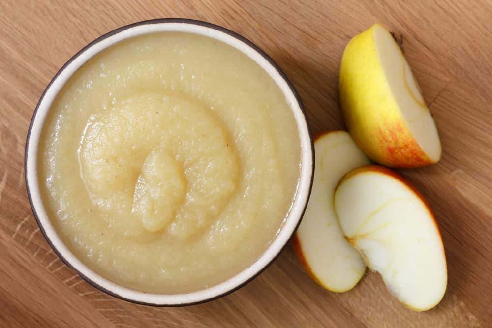 Apple sauce in rustic brown dish on dark wood. Sliced apples.