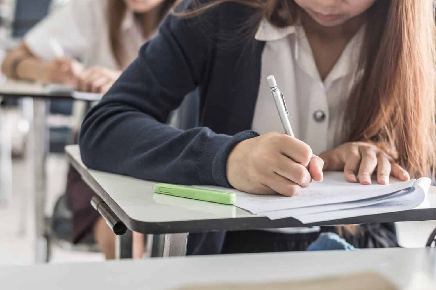 School student's taking exam writing answer in classroom for education and literacy concept