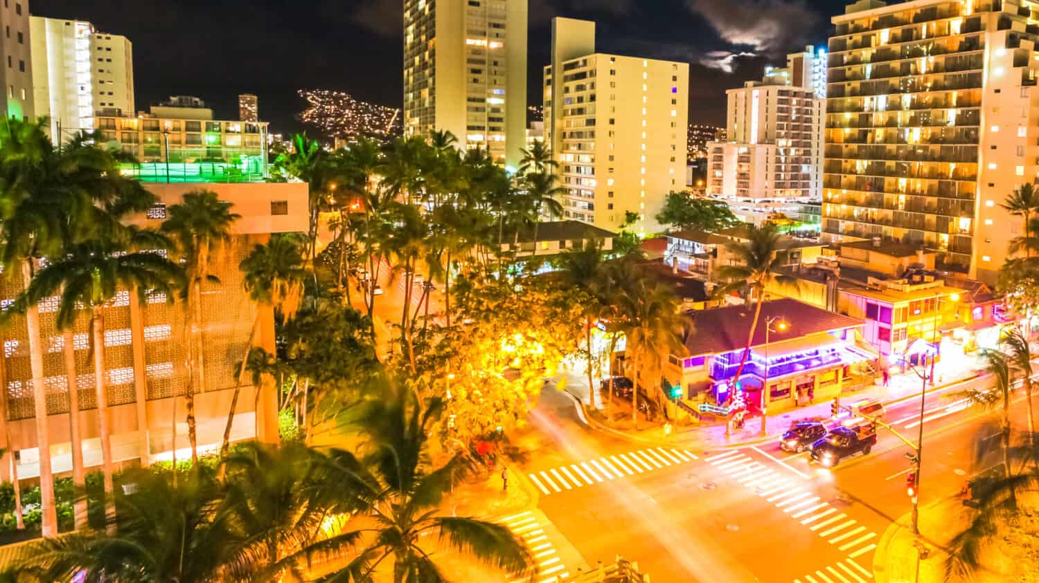 Aerial view night traffic of Waikiki city in Oahu, Hawaii, United States. Moving people and car glowing trails in the street. City night lights of shops and nightlife concept