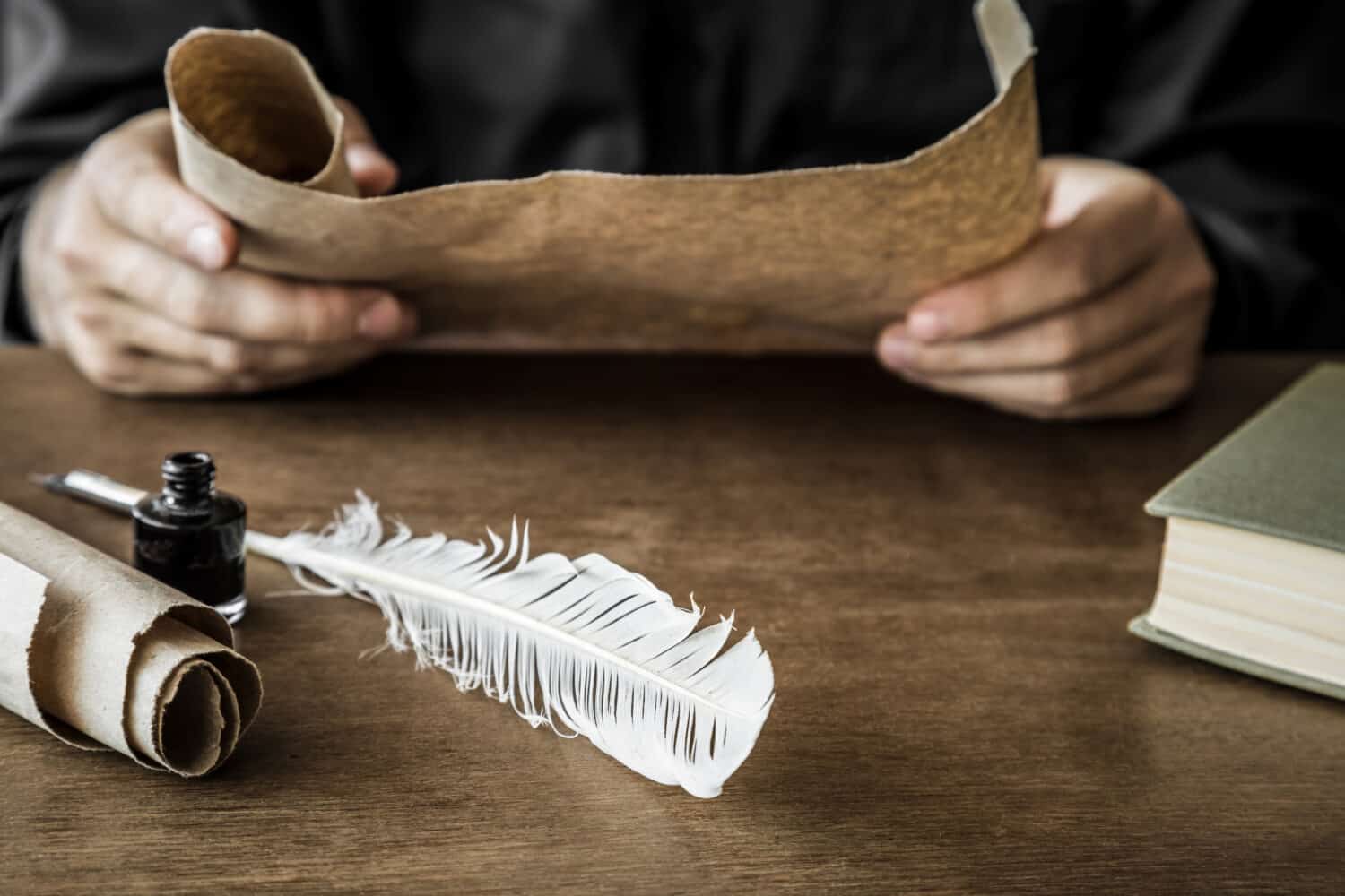 Man reading an old letter. Old quill pen, book and papyrus scroll on the wooden table. Historical atmosphere.