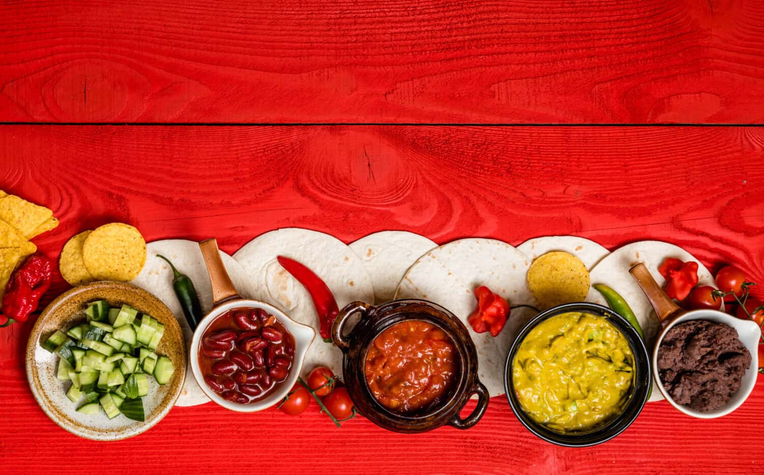 Mexican food concept: tortilla chips, guacamole, salsa, chilli, refried black beans, and fresh ingredients over vintage red rustic wooden background. vegetarian. Top view