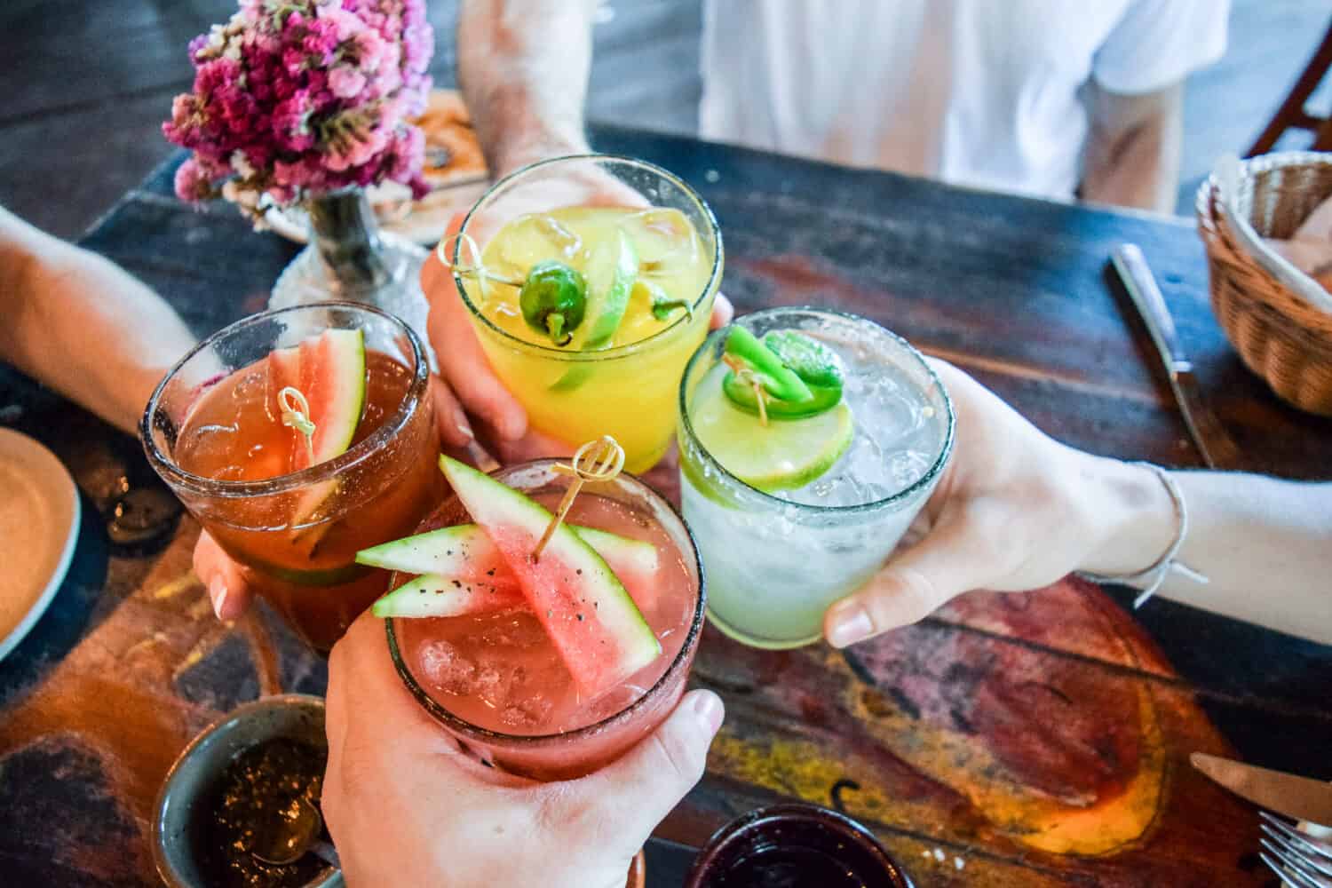 Friends toasting, saying cheers holding tropical blended fruit margaritas.  Watermelon and passionfruit drinks.