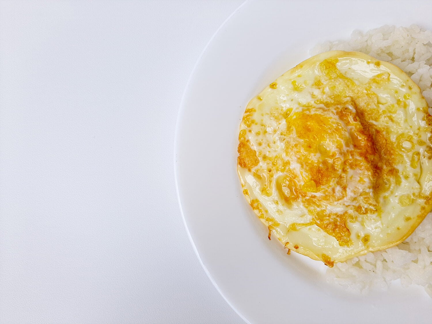 Fried egg or overcooked sunny side up, served with white rice, on a white plate, isolated in white background. Space for text. Flat lay or overhead