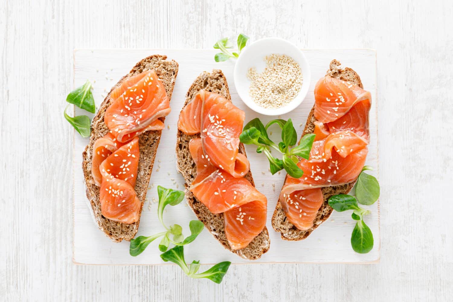 Whole grain rye bread open sandwiches with salted salmon on a white rustic wooden table. Healthy food. Top view