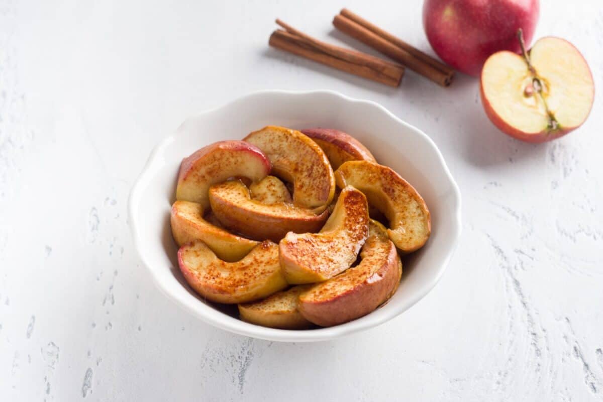 A white bowl of baked apple slices with cinnamon on a light blue background. Delicious homemade vegan dessert