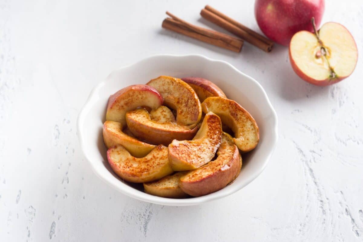 A white bowl of baked apple slices with cinnamon on a light blue background. Delicious homemade vegan dessert