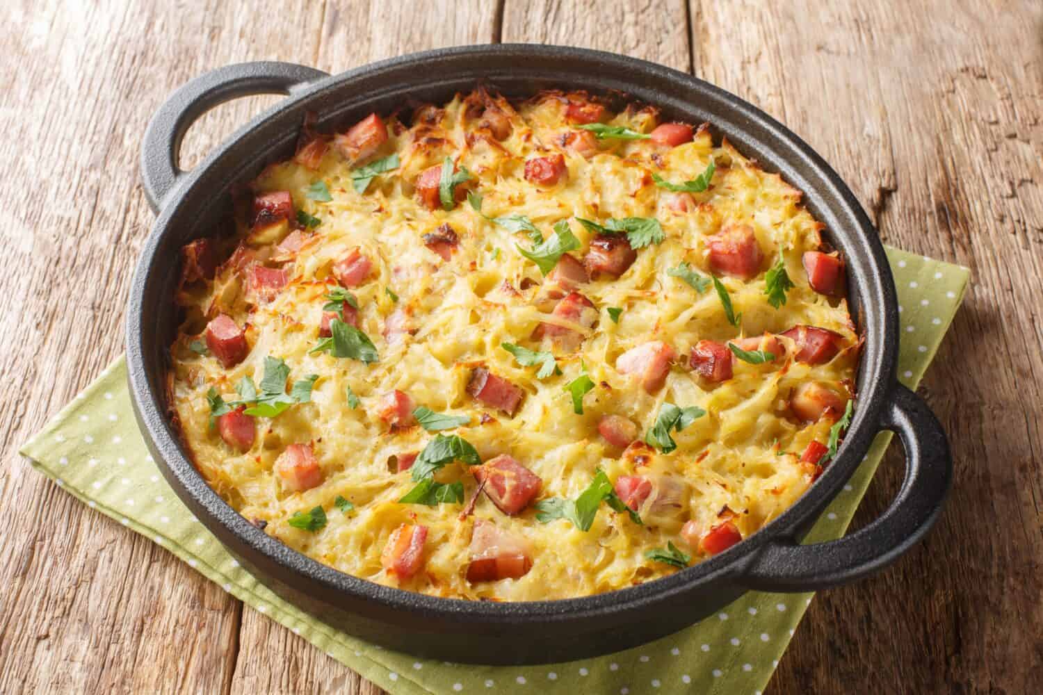 Hash brown of grated potatoes, leeks, eggs and diced smoked bacon close-up in a pan on the table. Horizontal