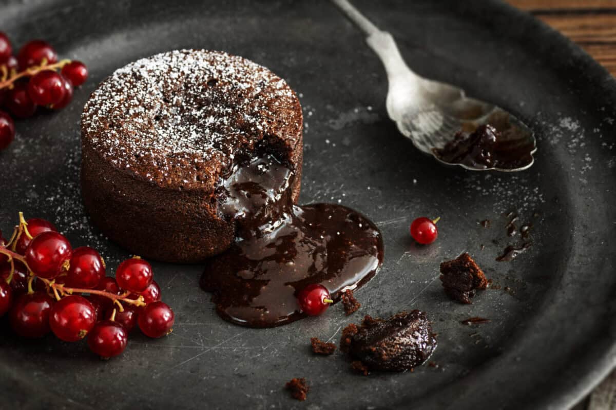 Warm Chocolate Lava Cake with Bite Taken Out of Molten Center and Red Currants on Vintage Metal Plate