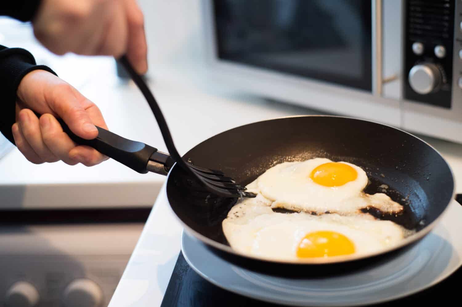 Unrecognizable man preparing fried eggs for breakfast. Close up.