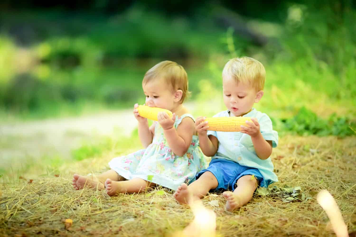 Two cute kids in the woods eating corn