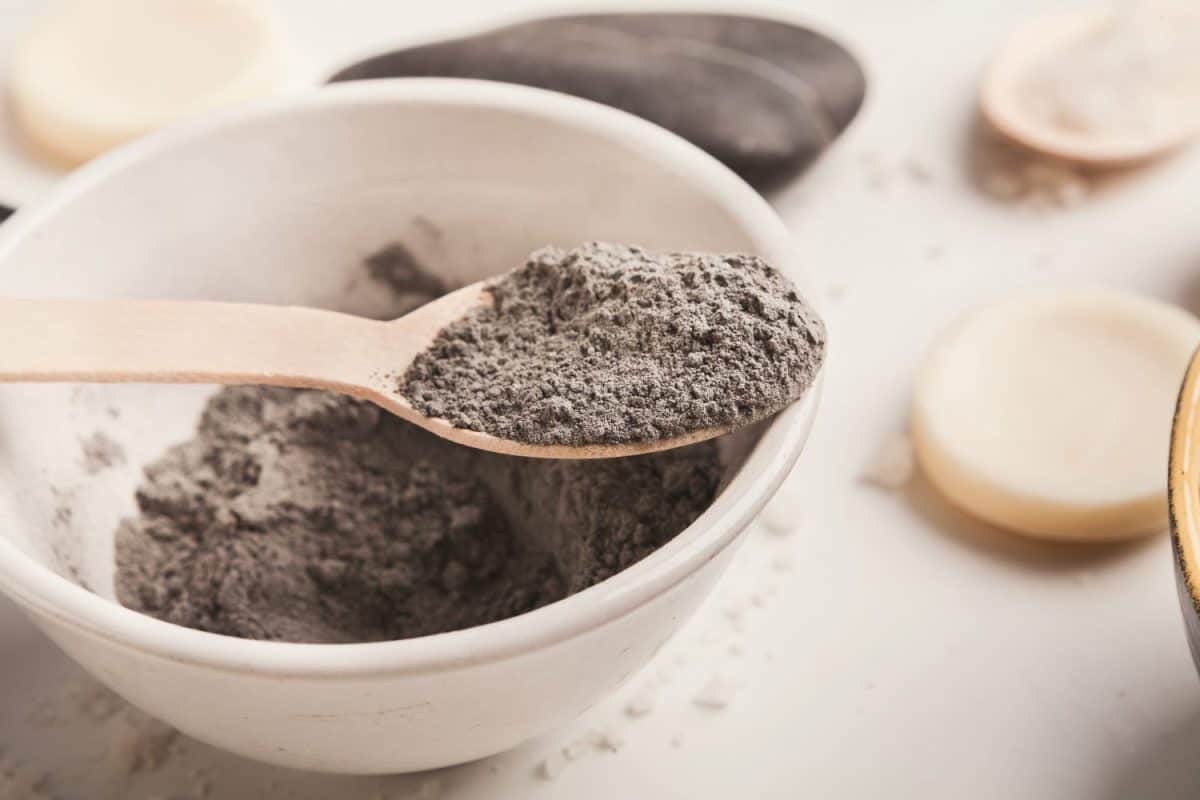 Preparing cosmetic black mud mask in bowl on white background with various skin care products. Closeup texture of dry facial clay powder. Natural cosmetics for home or salon spa treatmentShampoo clay treatment for diaper rash
