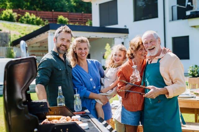 Multi generation family grilling outside on backyard in summer during garden party