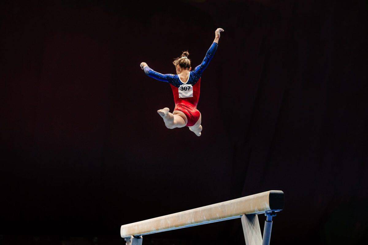 woman exercise on balance beam gymnastics, perform split jump on black background. The best extra-curricular activities for creative kids